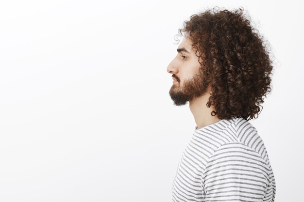 Foto gratuito ritratto di profilo di bel ragazzo ispanico con barba e capelli ricci, guardando da parte mentre in piedi senza emozioni