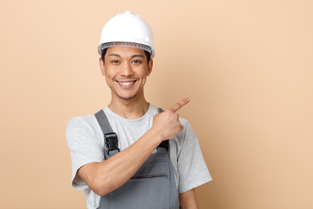 Foto gratuito sorridente giovane operaio edile indossando il casco di sicurezza e uniforme rivolto verso l'alto all'angolo