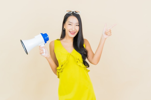 Foto gratuito sorriso della bella giovane donna asiatica del ritratto con il megafono sulla parete di colore