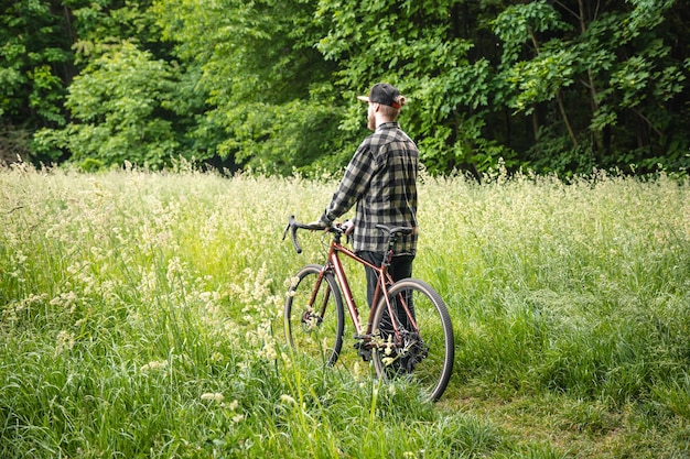 Foto gratuito un giovane con una bicicletta nella foresta tra l'erba