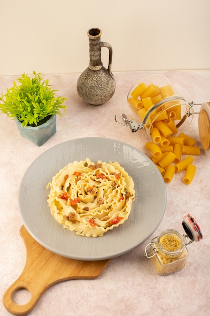 Foto gratuito un pasto gustoso di pasta italiana vista dall'alto con verdure cotte e fettine di carne all'interno della lastra grigia insieme a fiori e pasta cruda sul rosa