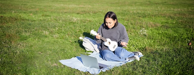 Foto gratuito una graziosa musicista asiatica che studia guarda il tutorial sul suo laptop un tutor online le mostra come suonare