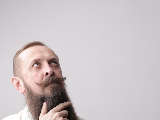 Foto gratuito uomo con una lunga barba e baffi in piedi davanti a un muro grigio