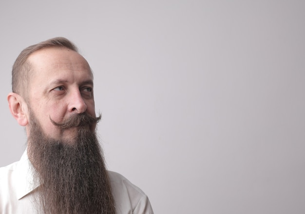 Foto gratuito uomo con una lunga barba e baffi in piedi davanti a un muro grigio