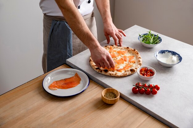 Uomo di alto angolo che mette le fette di salmone affumicato sulla pasta della pizza al forno