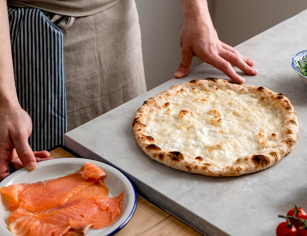 Uomo di alto angolo in piedi vicino a pasta per pizza al forno e fette di salmone affumicato