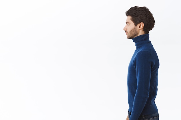 Foto gratuito uomo in maglione blu a collo alto, in piedi dritto con espressione determinata e assertiva, posa sfondo bianco senza emozioni