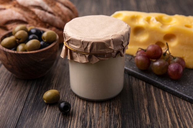 Foto gratuito vista frontale del formaggio maasdam con uva su un supporto e olive con yogurt sul tavolo