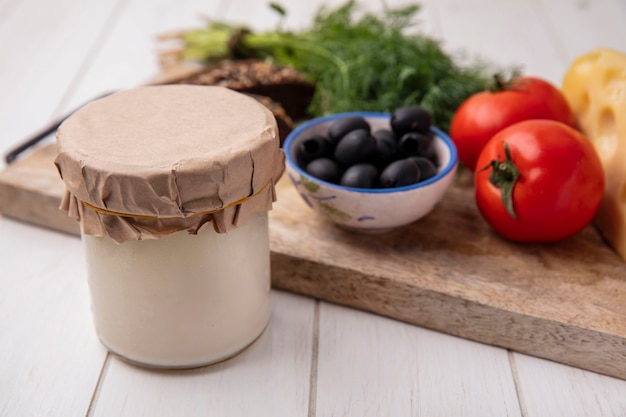 Foto gratuito vista frontale yogurt in un barattolo con olive pomodori fette di pane integrale e aneto su un supporto su uno sfondo bianco