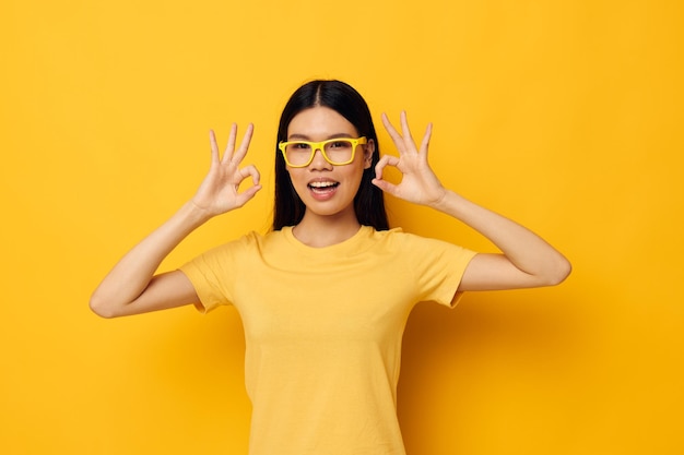 Foto affascinante giovane donna asiatica con gli occhiali che gesturing con le mani copyspace sfondo giallo inalterato