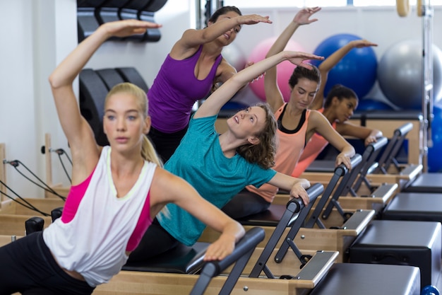 Allenatore femminile che assiste un gruppo di donne con esercizi di stretching sul riformatore