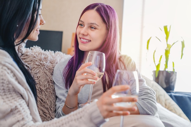 Amici sorridenti felici delle giovani donne che aprono bottino di vino a casa e lo bevono