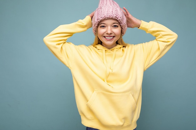 Foto attraente giovane donna bionda felice sorridente in piedi isolata sopra la parete di fondo colorata che indossa abiti alla moda di tutti i giorni che mostrano le emozioni del viso che guarda l'obbiettivo.