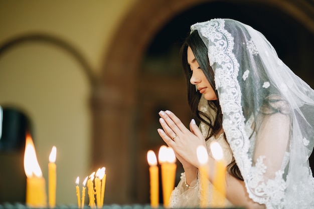 Foto bella sposa in chiesa che prega accanto alle candele dopo la cerimonia del matrimonio