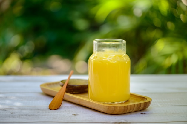 Burro di ghee in barattolo di vetro con spatola di legno su tavolo di legno bianco con sfondo verde sfocato.