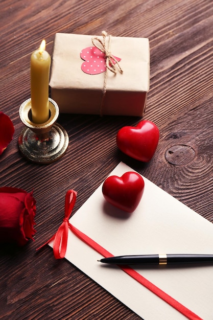 Carta regalo per San Valentino con scatola rosa rossa penna e candela su sfondo di legno