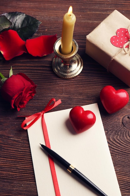 Carta regalo per San Valentino con scatola rosa rossa penna e candela su sfondo di legno