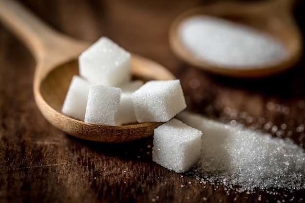 Foto chiuda sui cubi e sulla canna dello zucchero in cucchiaio di legno sulla tavola