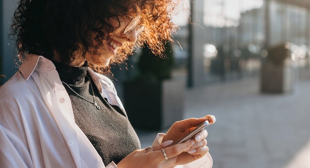 Close up ritratto di una donna caucasica con i capelli ricci in chat con qualcuno mentre posa fuori con gli occhiali