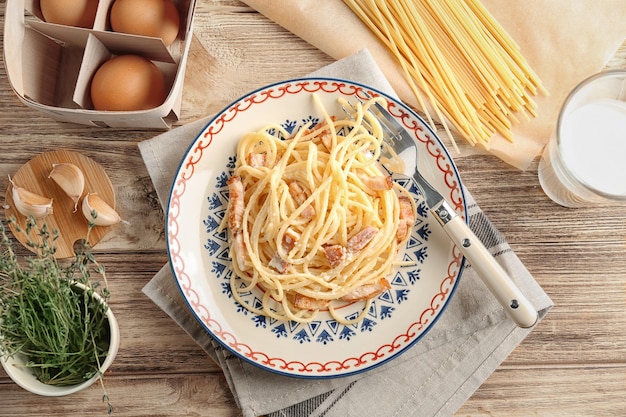 Composizione con piatto di pasta alla carbonara e pancetta sul tavolo