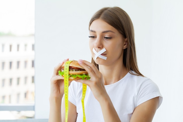 Concetto di dieta donna carina con la bocca sigillata mantiene hamburger grasso