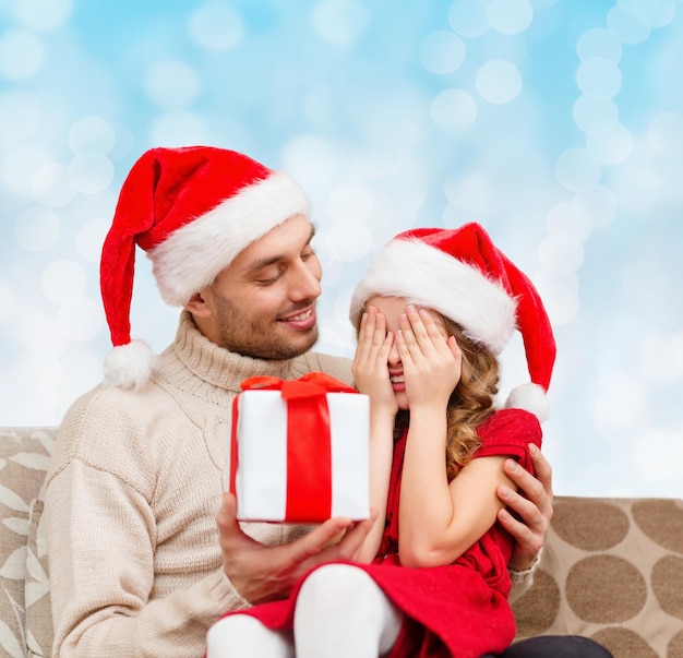 concetto di famiglia, natale, vacanze invernali e persone - figlia sorridente con gli occhi chiusi in attesa del regalo del padre su sfondo di luci blu