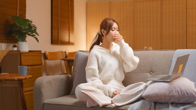 Concetto di stile di vita domestico Giovane donna assonnata e che sbadiglia mentre lavora al computer portatile a tarda notte d'inverno