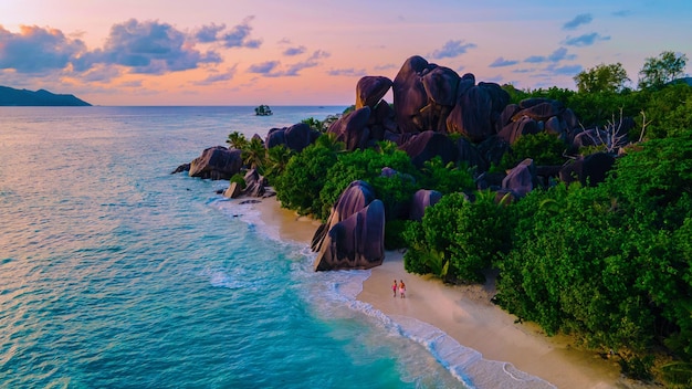 Foto coppia di uomini e donne che camminano sulla spiaggia durante il tramonto in una vacanza di lusso alle seychelles