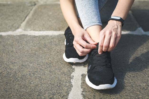 Corridore della ragazza che lega i lacci per fare jogging le scarpe sulla strada in un parco