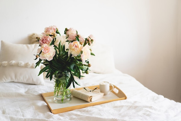 Dettagli di natura morta nell'interno della casa del soggiorno Libro aperto con bicchieri tazza di caffè e bouquet fiori di peonie rosa bianche leggere e riposare Casa accogliente