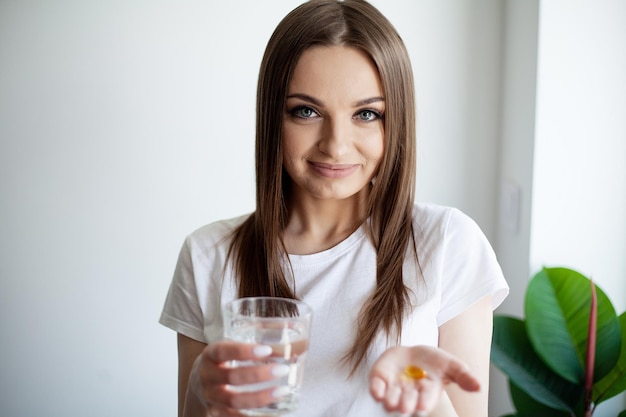 Donna che prende la pillola della vitamina con un bicchiere di acqua dolce all'interno