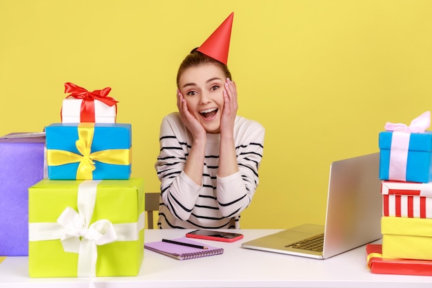 Donna seduta sul posto di lavoro tra le scatole presenti che indossano un cono di festa che celebra il suo compleanno al lavoro