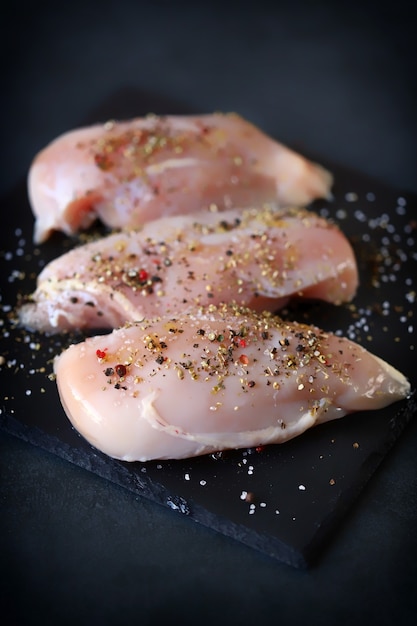 Filetti di pollo crudi con spezie su una tavola di pietra.