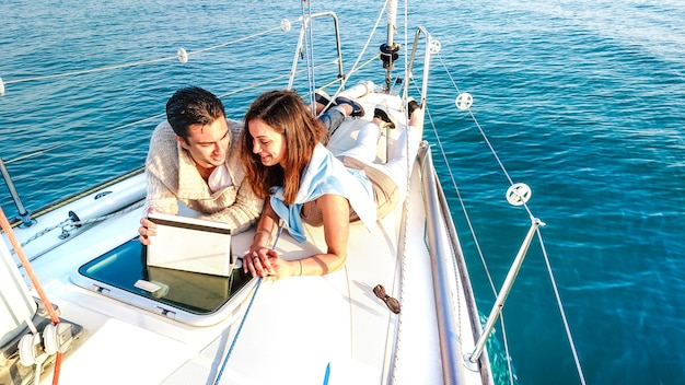 Giovane coppia innamorata che si diverte con il tablet pc sulla barca a vela - Stile di vita di viaggio di lusso e concetto di nomade digitale su un esclusivo tour in yacht - Filtro vivido luminoso con distorsione morbida dell'obiettivo fisheye