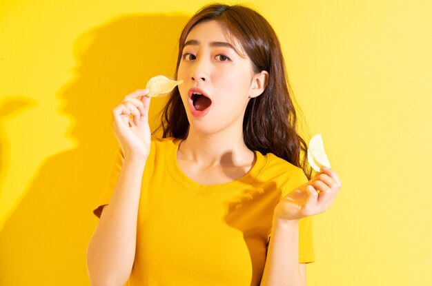 Foto giovane ragazza asiatica che mangia spuntino su colore giallo