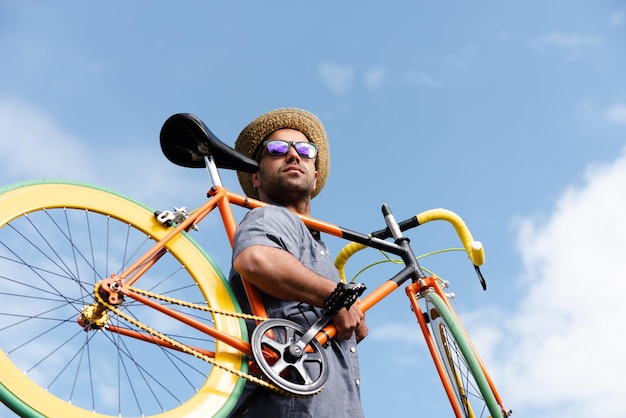 Foto hipster ispanico che porta una bicicletta fissa colorata sulla spalla con un cielo blu come sfondo