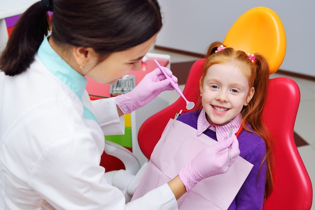 Il bambino è una bambina dai capelli rossi che sorride seduto su una poltrona del dentista. Odontoiatria pediatrica, denti da latte