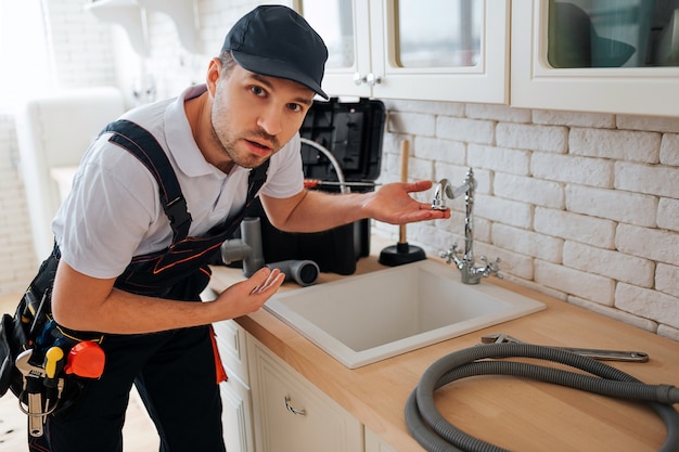 Foto il giovane stupito considera la macchina fotografica e indica il lavandino in cucina