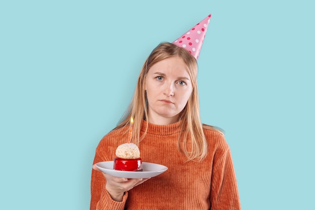 Il ritratto di una donna degli anni '20 ha un'espressione del viso insoddisfatta indossa abiti festivi festeggia il compleanno tiene una gustosa torta isolata su sfondo blu