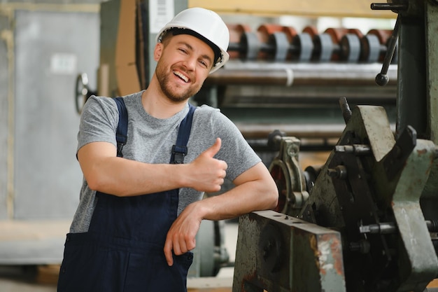 Foto impiegato sorridente e felice operaio industriale al chiuso in fabbrica giovane tecnico con elmetto bianco