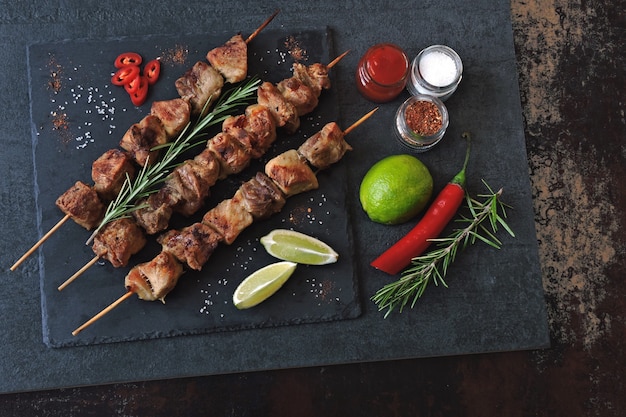 Kebab appetitoso con spezie, peperoncino e lime. Spiedini di maiale profumati su una tavola di pietra.