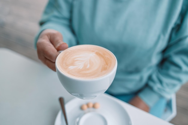 La donna passa tenendo una tazza bianca di caffè latte in piedi sul tavolo mentre si rilassa in una caffetteria