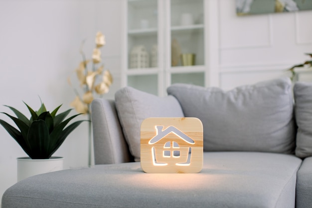 Foto lampada da notte in legno con foto di casa, sul divano monocromatico grigio, all'interno del salotto di casa luce elegante