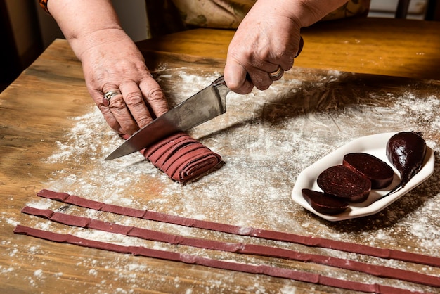 Mani che tagliano tagliatelle viola con ingredienti sul tavolo cibo italiano fatto in casa