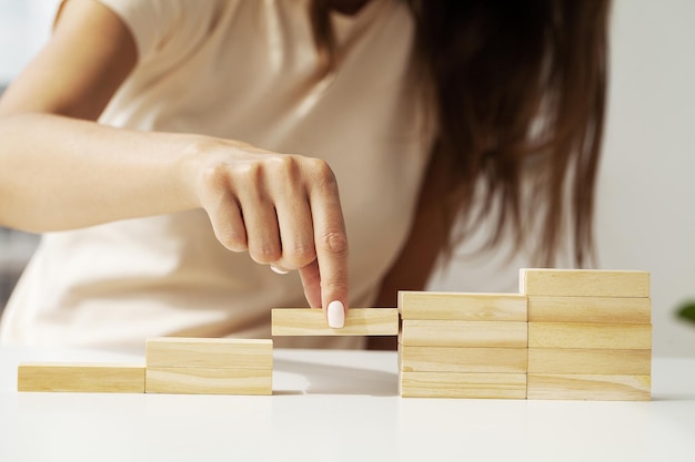 Mano della donna che organizza l'impilamento del cubo di legno come forma del gradino della scala