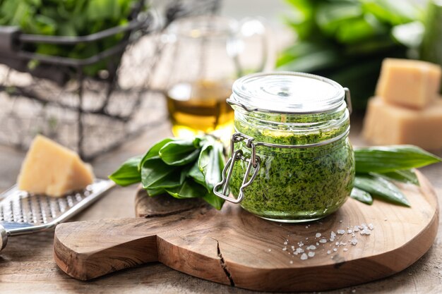 Foto pesto di porri selvatici con olio d'oliva e parmigiano in un barattolo di vetro su un tavolo di legno. proprietà utili di aglio orsino. foglie di aglio orsino fresco.