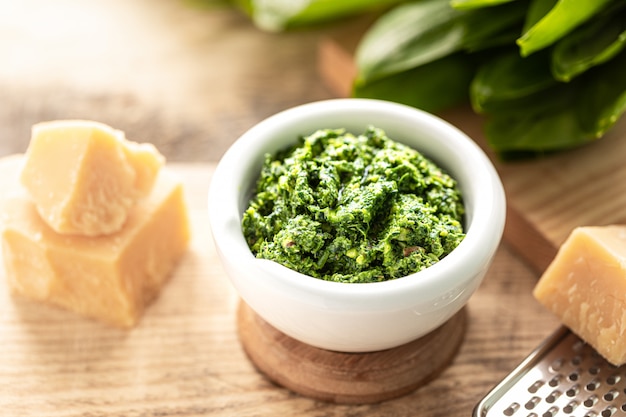 Foto pesto di porri selvatici con olio d'oliva e parmigiano in un mortaio di ceramica bianca su un tavolo di legno. proprietà utili di aglio orsino.