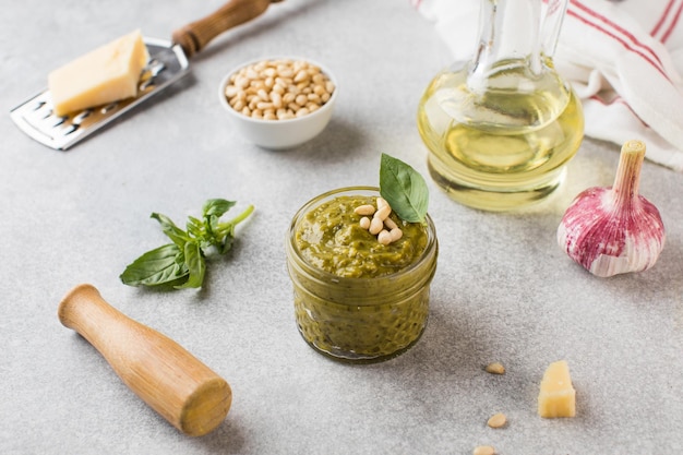 Foto pesto in vasetto con un pezzo di parmigiano basilico foglie pinoli e olio d'oliva in bottiglia cucina italiana