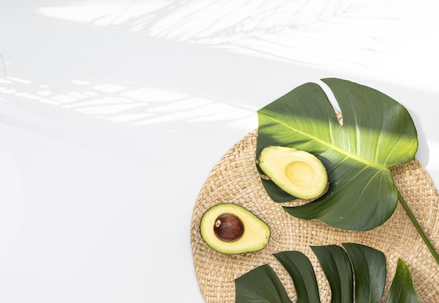 Pezzi di avocado su un pavimento di fibre naturali e ha uno sfondo di natura Foglia di monstera tropicale