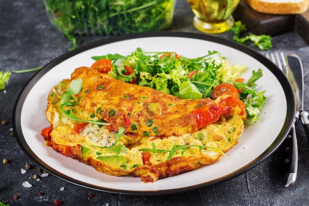 Prima colazione. Frittata con pomodori, avocado, gorgonzola e piselli verdi sul piatto bianco.